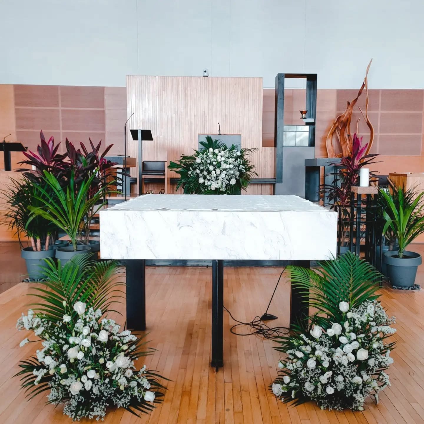 Wide front view of the church altar with white flowers and greenery arranged around the marble table