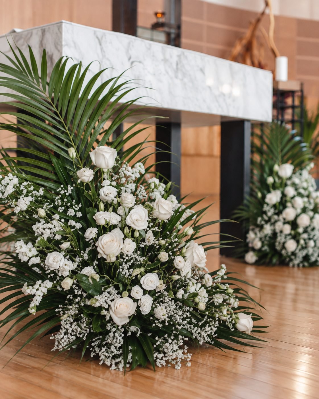 Close detail of a low white floral arrangement with palm leaves beside the marble altar