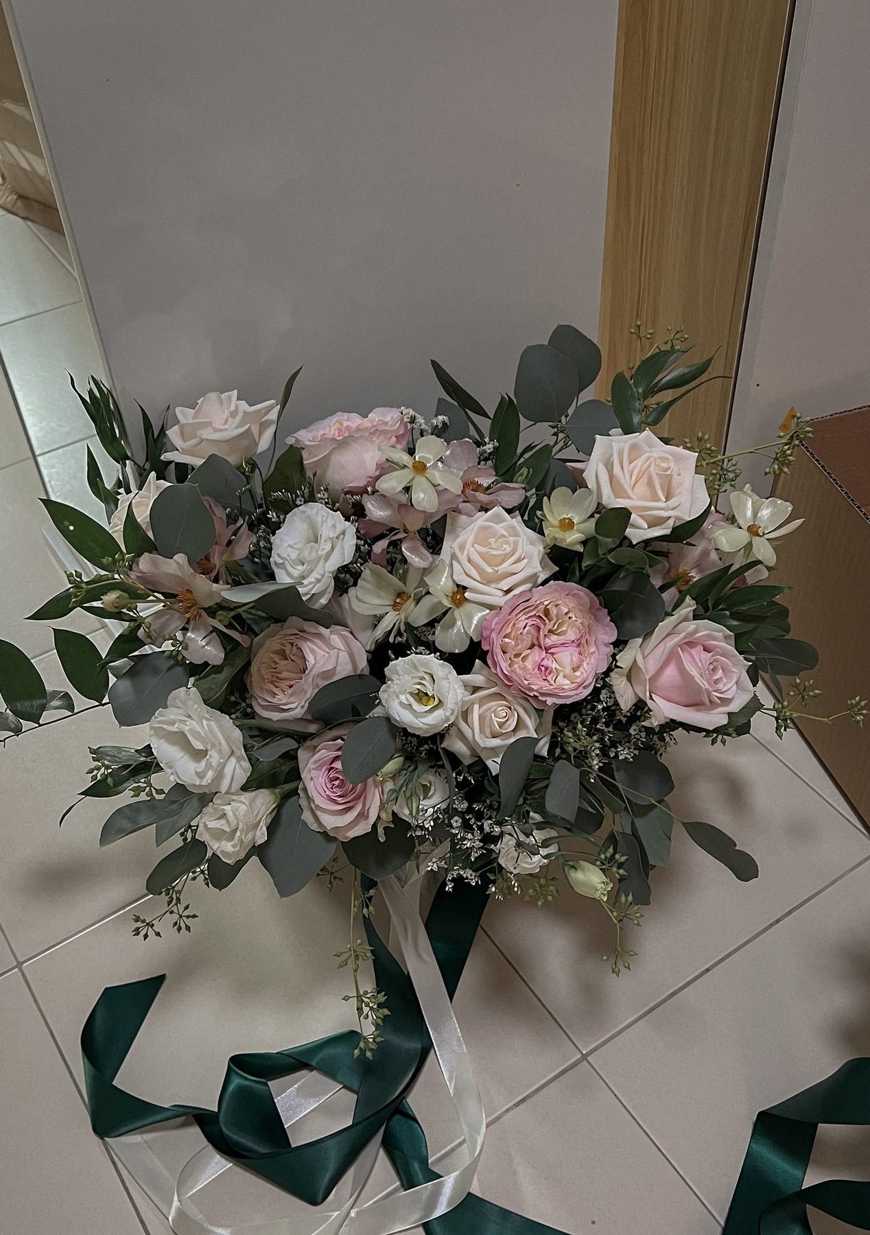 Blush, white and green bouquet with dark green and cream ribbons lying on a tiled floor
