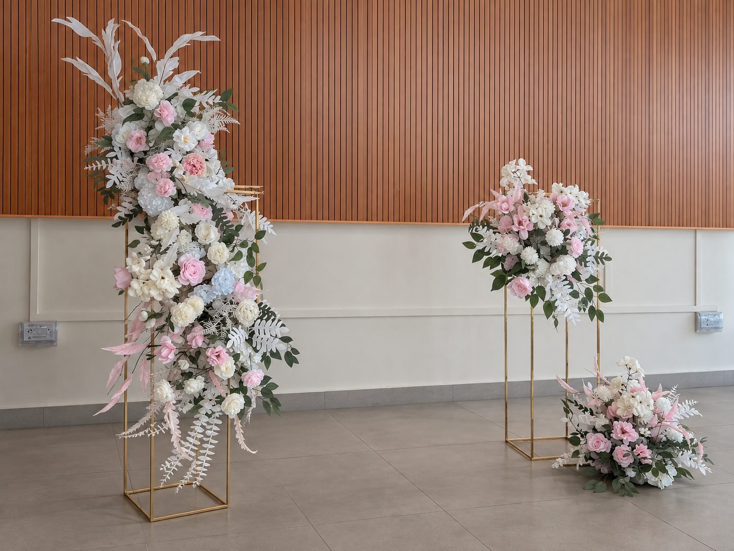 Gold frame stands with blush, white and green flowers and a low ground arrangement, angled view
