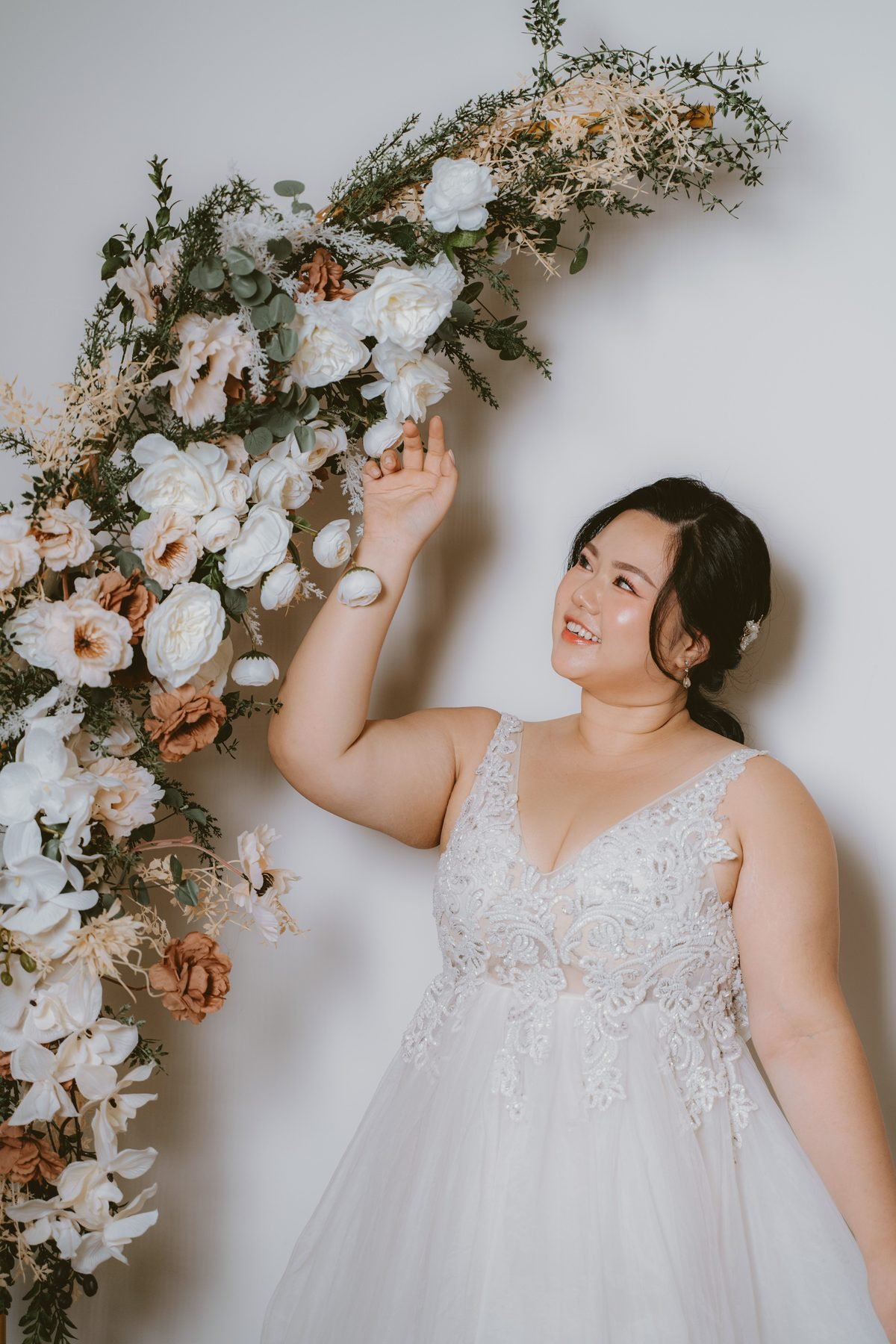 Bride reaching up to a white and cream floral arch with eucalyptus and dried roses