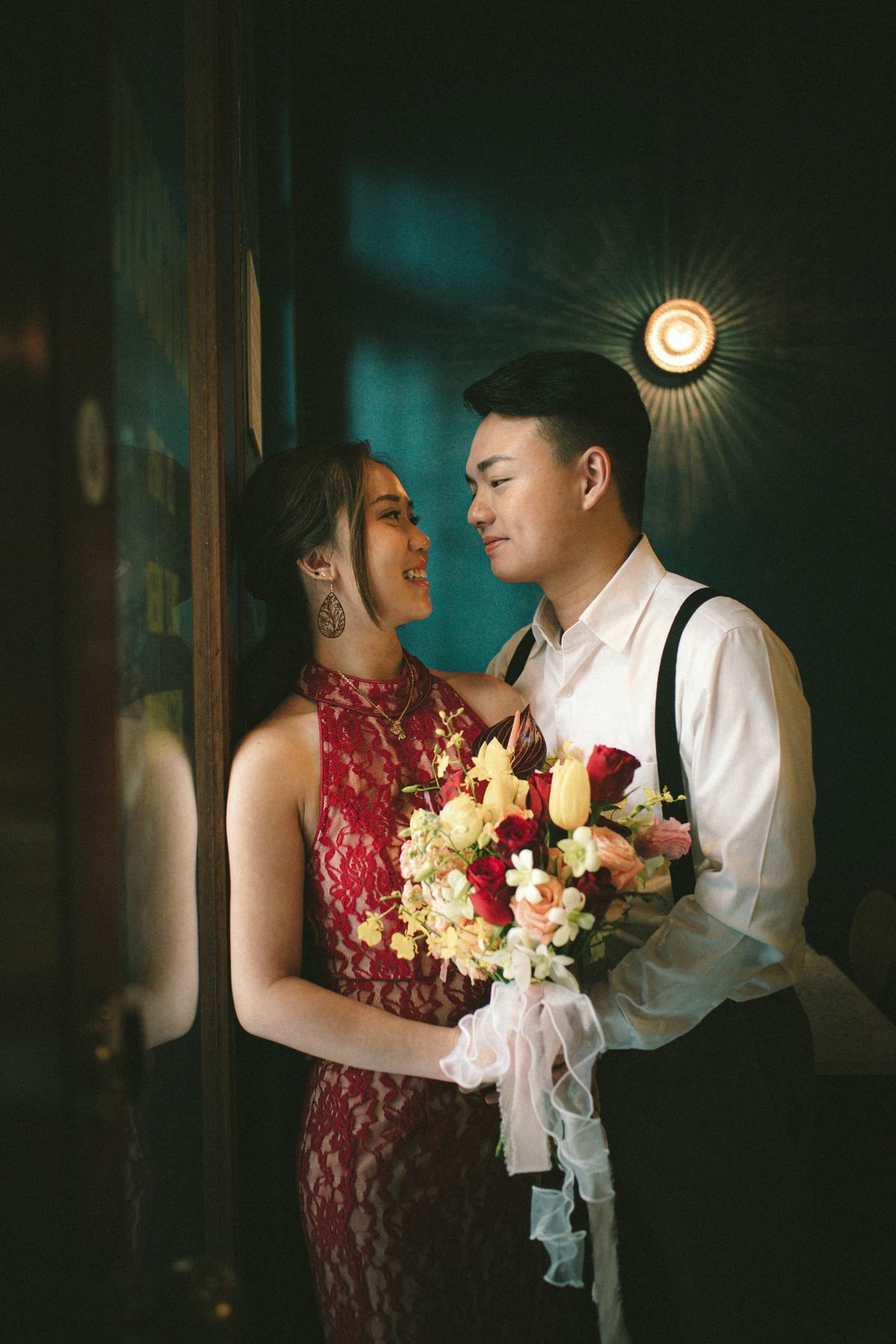 Couple holding a red, yellow and peach bouquet in a dark teal interior
