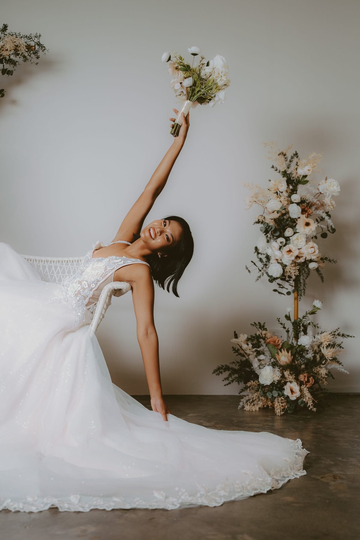 Bride reclining with a white bouquet beside a tall cream and blush dried arrangement